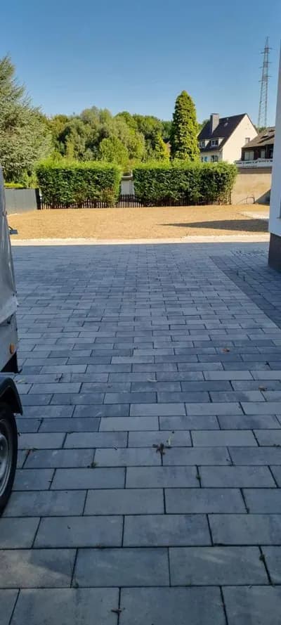 Gepflasterte Zufahrt mit angrenzender Rasenfläche und Hecke