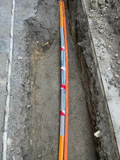 Orangefarbenes Glasfaser-Leerrohr im offenen Kabelgraben neben dem Gehweg