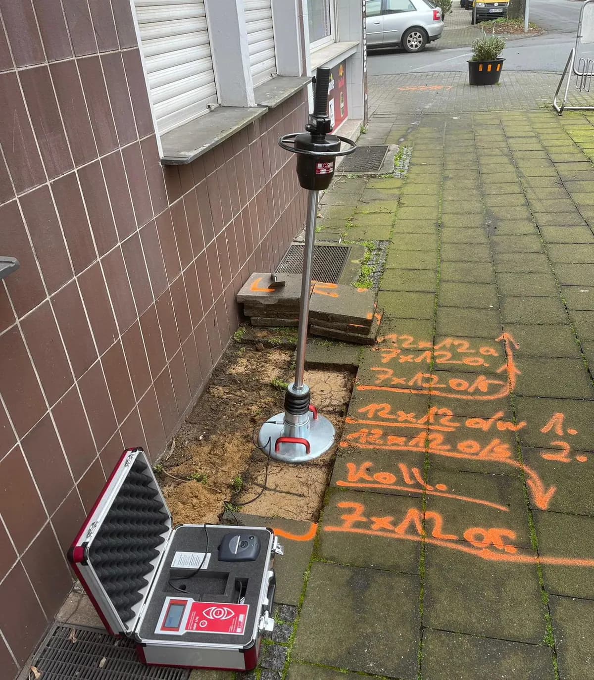 Vermessungsgerät und Bodenmarkierungen vor einer Hauswand vor dem Hausanschluss