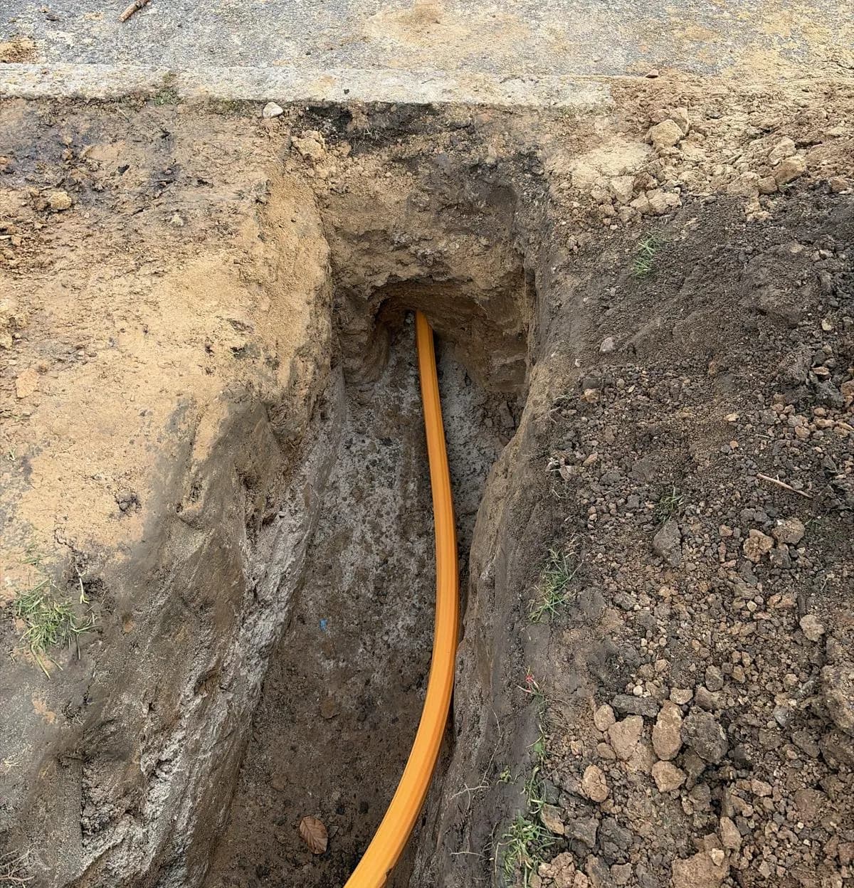 Orangefarbenes Leerrohr in der Aufgrabung unter der Asphaltdecke