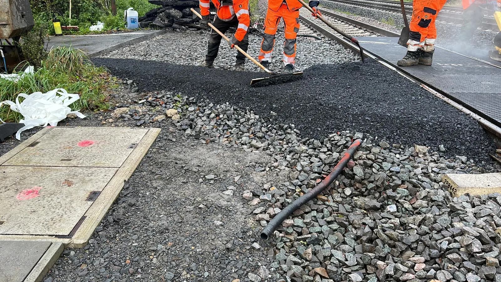Bauarbeiter in Warnkleidung verdichten Asphalt an einem Gleisübergang