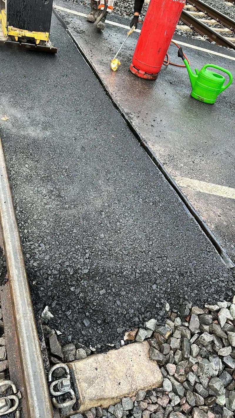 Frisch eingebaute Asphaltdecke unmittelbar neben dem Gleisbett