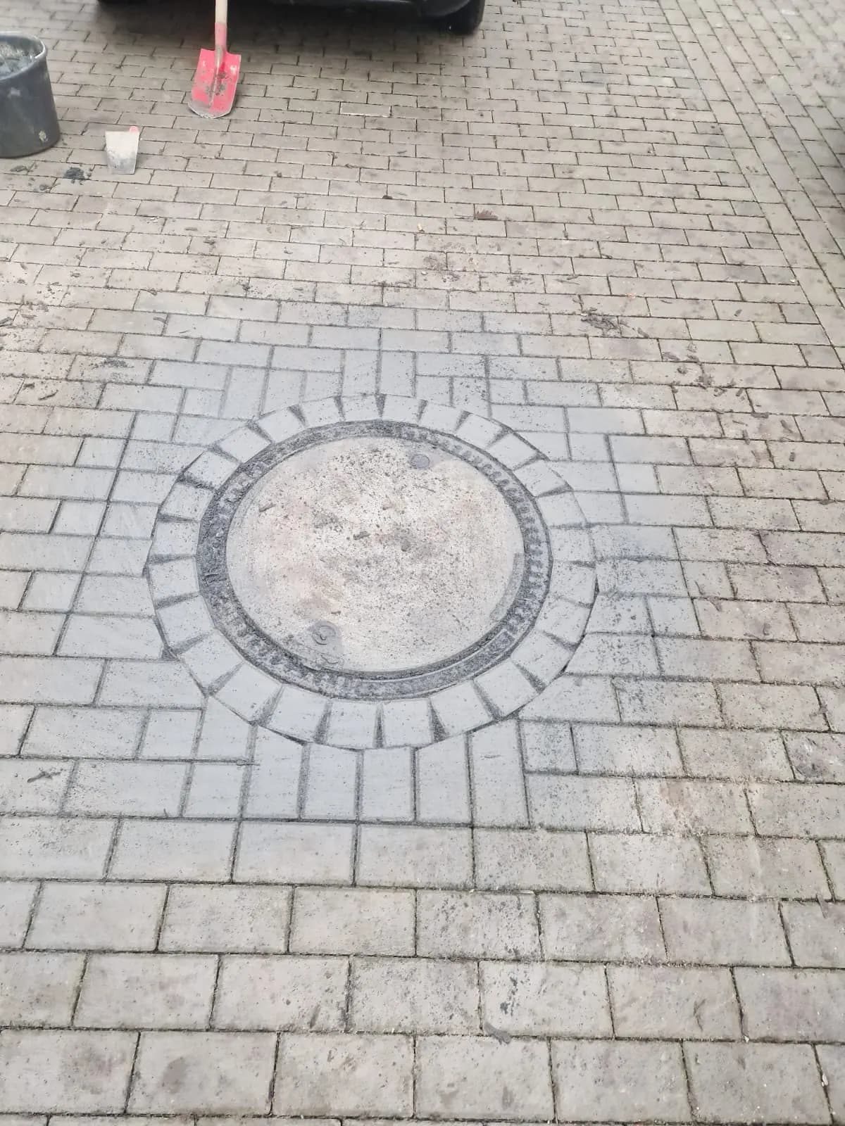 Detailaufnahme eines runden Kanalschachts im Betonsteinpflaster