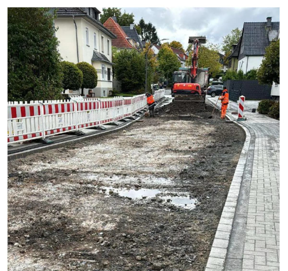 Straßenbaustelle im Wohngebiet mit Absperrung, Bagger und neuer Pflasterkante