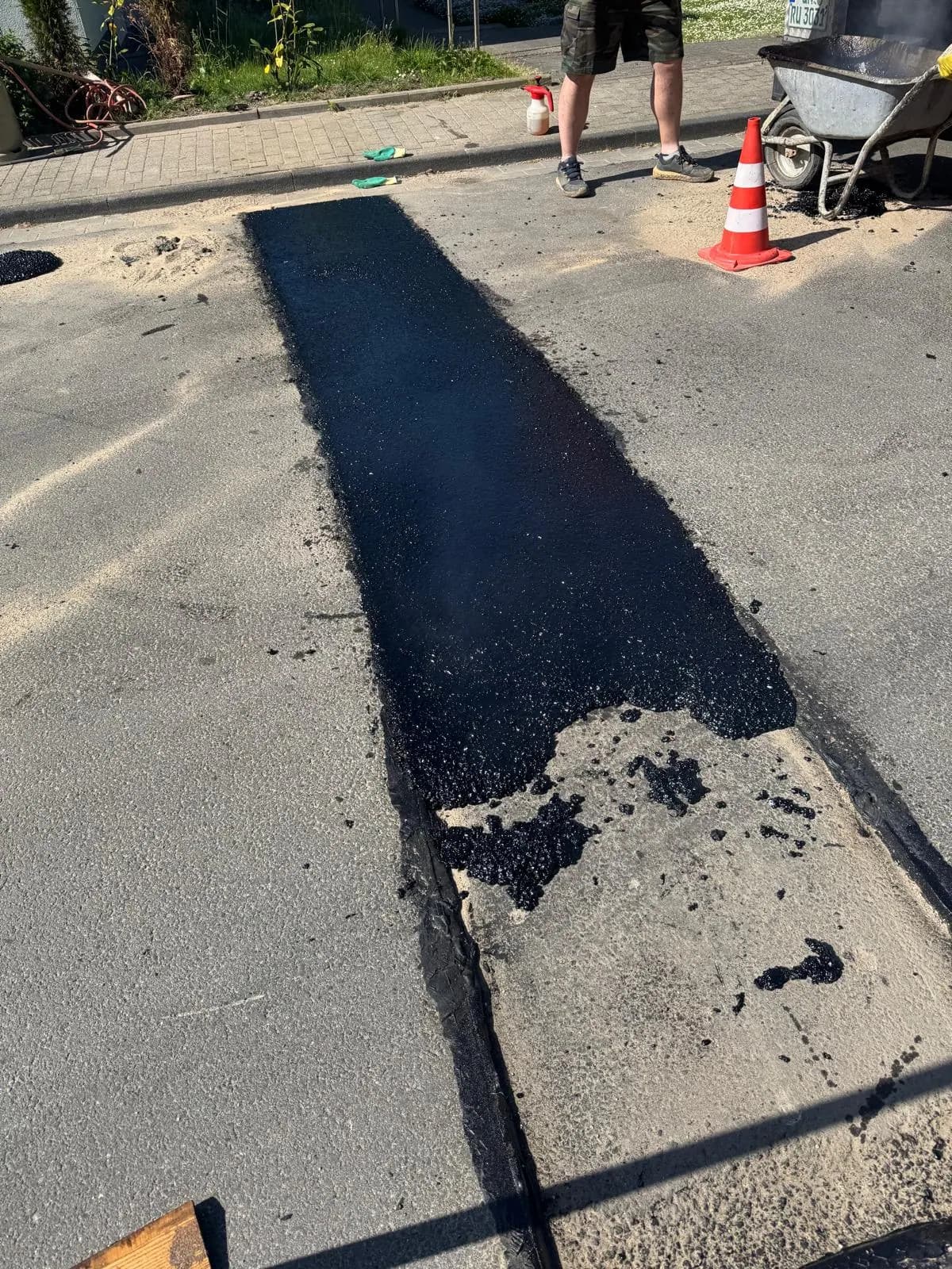 Frisch eingebaute Asphaltfläche in einer Wohnstraße, im Hintergrund Arbeiter mit Schubkarre