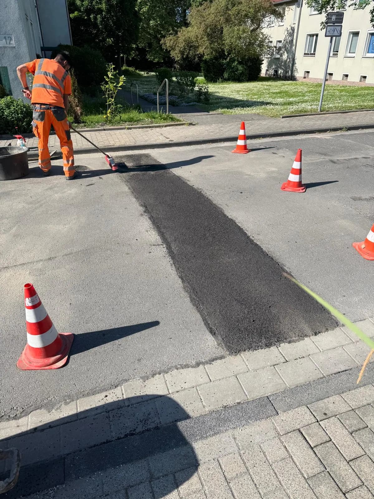 Arbeiter in Warnkleidung glättet eine Asphaltausbesserung neben dem Gehweg