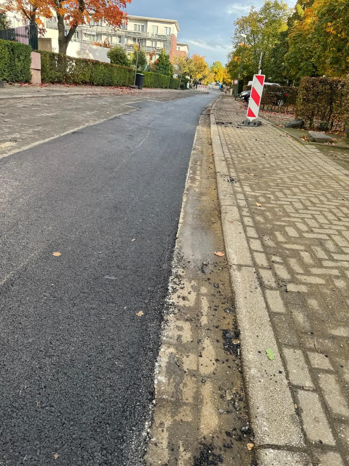 Asphaltstreifen neben Pflasterrinne mit Absperrbake