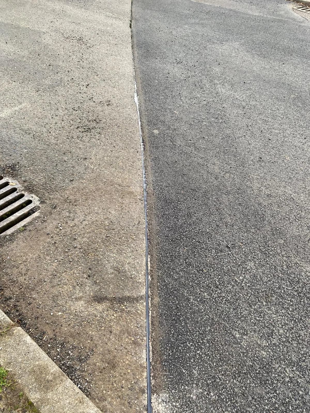 Neu eingebaute Asphaltbahn neben Bordstein und Straßeneinlauf