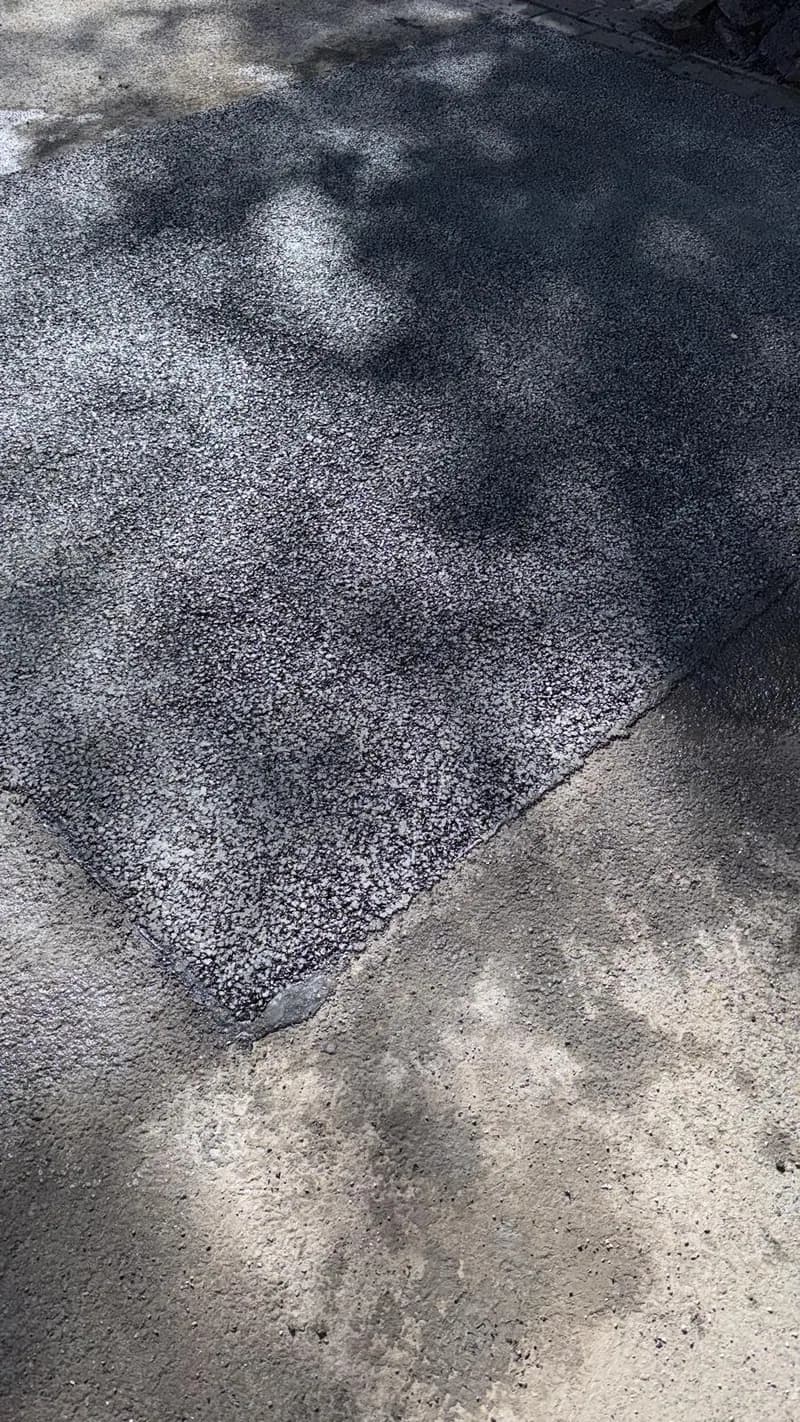 Ausgebesserte Asphaltfläche im Schatten von Bäumen