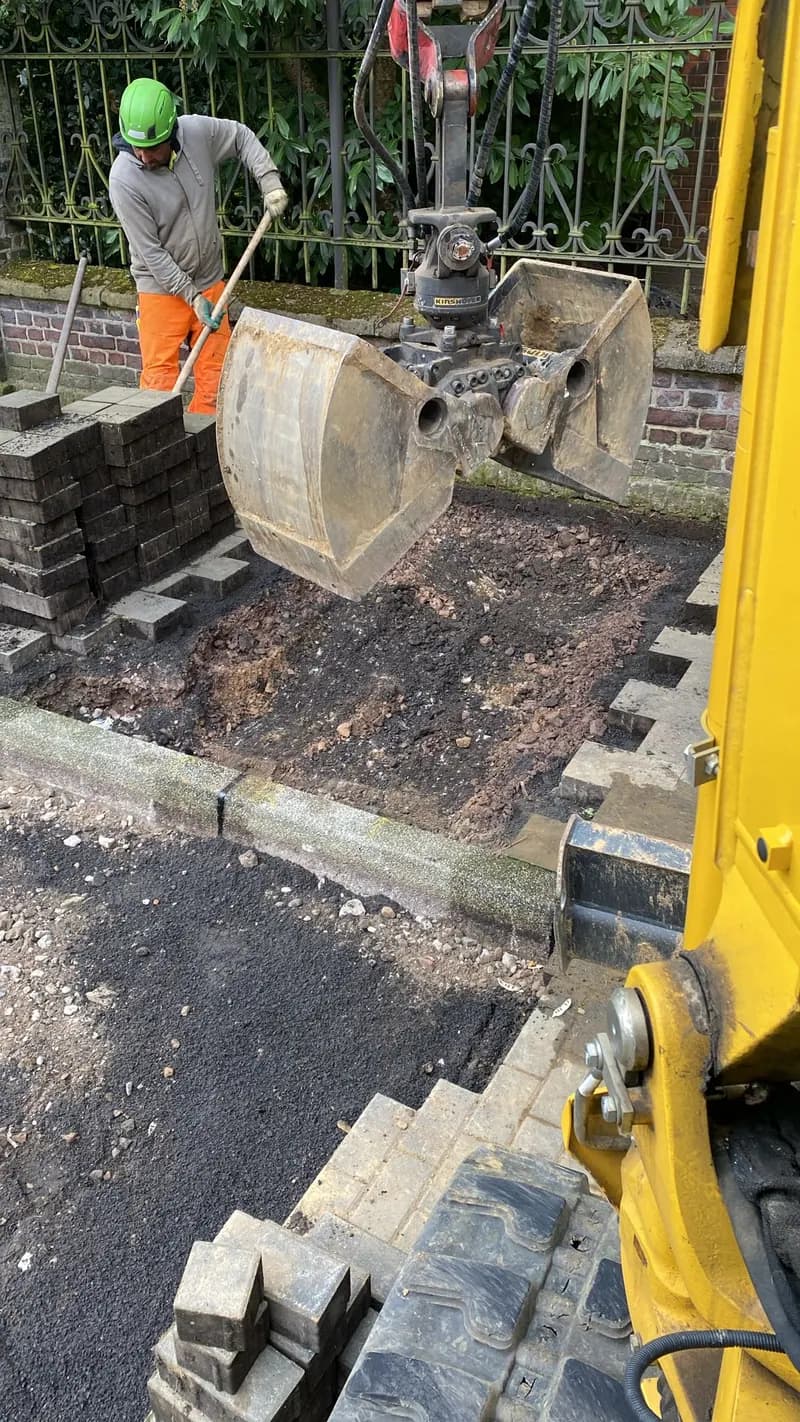 Arbeiter setzt Pflastersteine neben einem Bagger auf der Baustelle