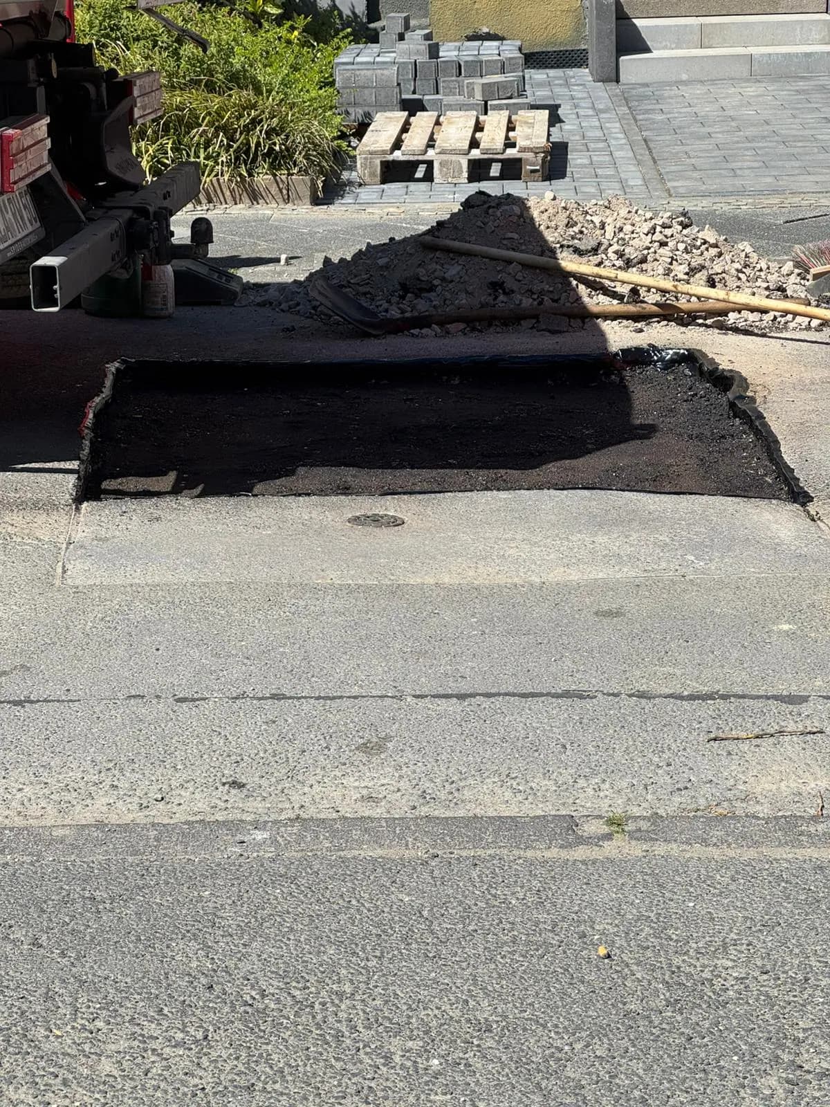 Aufgebrochene Asphaltdecke mit Pflastersteinpaletten vor der Wiederherstellung