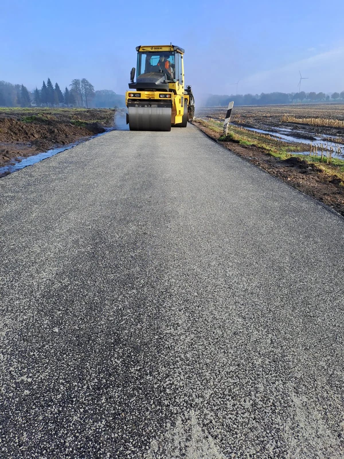 Walze verdichtet die Asphaltdecke eines Wirtschaftswegs