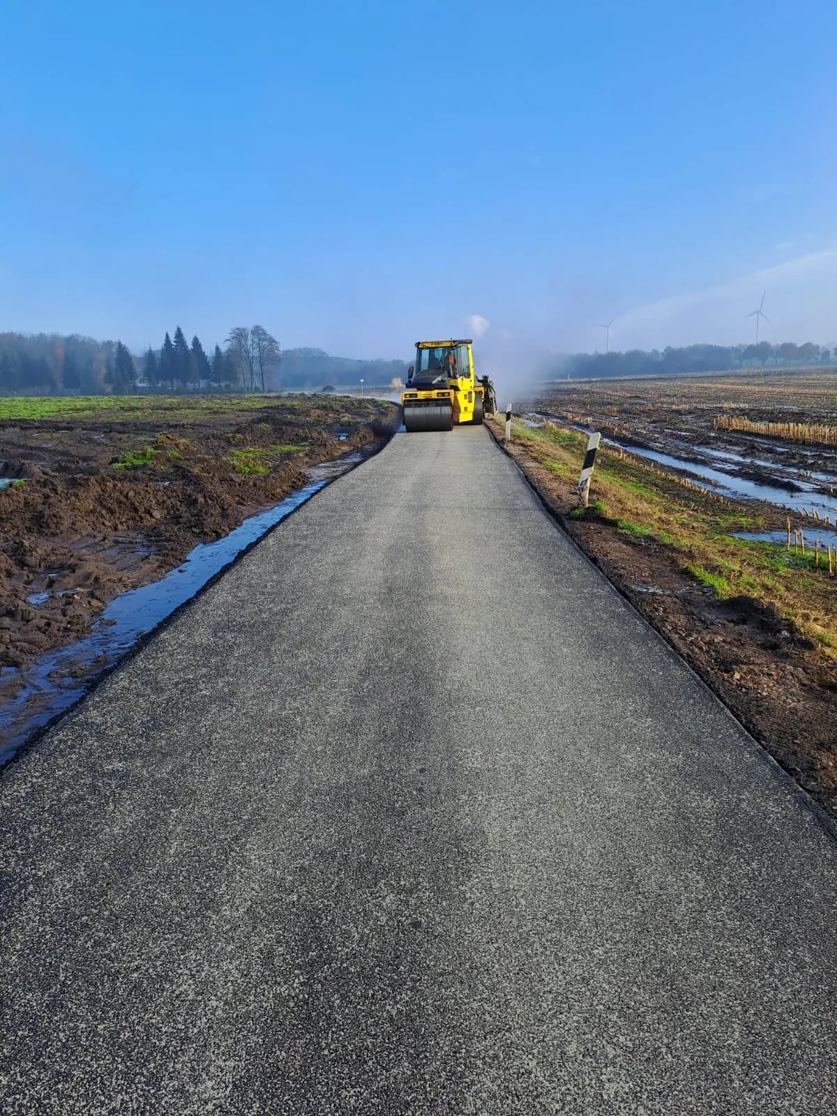 Neu gebauter Weg durch Ackerland mit Walze im Hintergrund