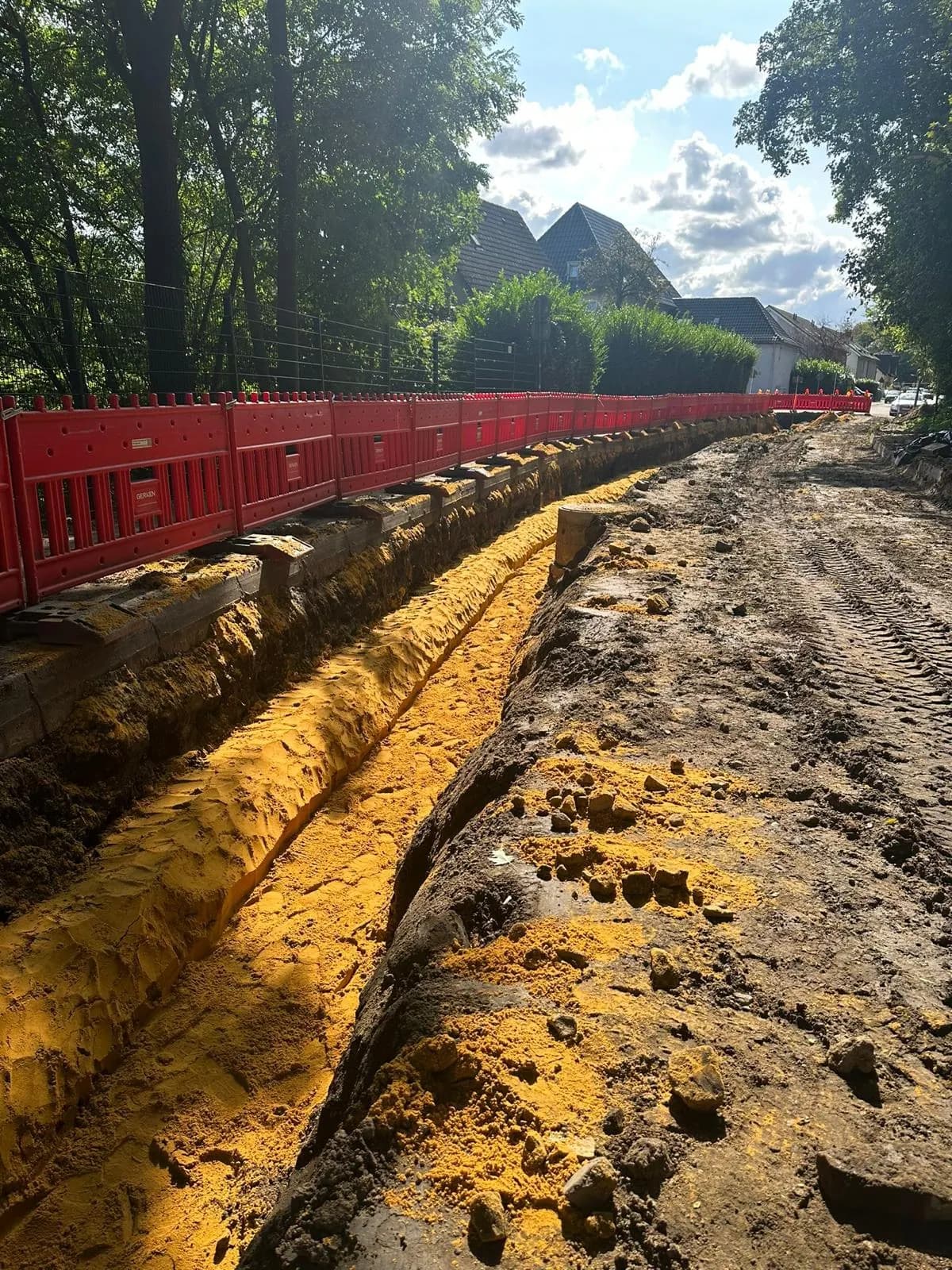 Ausgehobener Graben entlang eines Fußwegs mit Absperrung