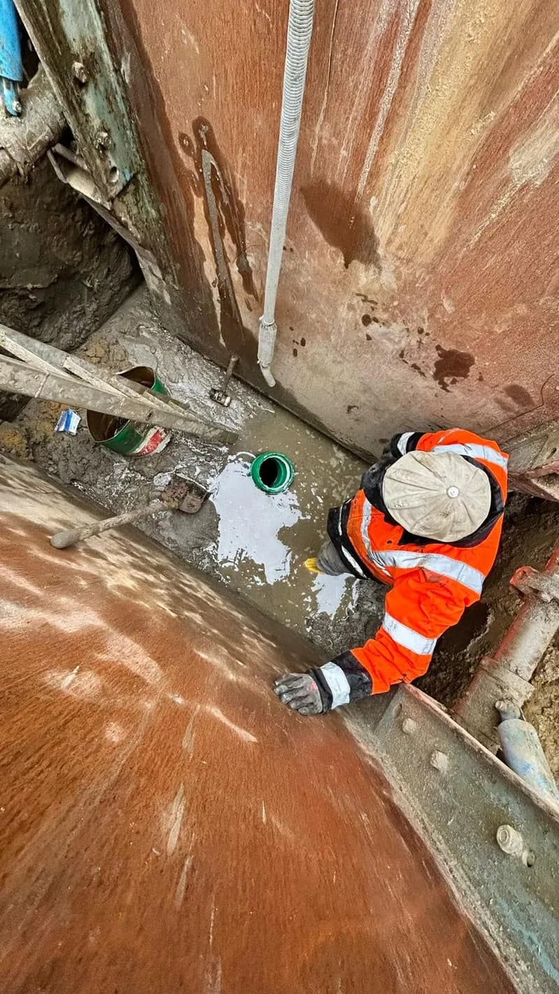 Arbeiter in Warnkleidung montiert einen Anschluss im Schachtbauwerk