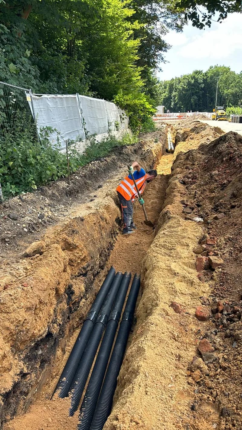 Arbeiter verlegt Leerrohre im offenen Graben