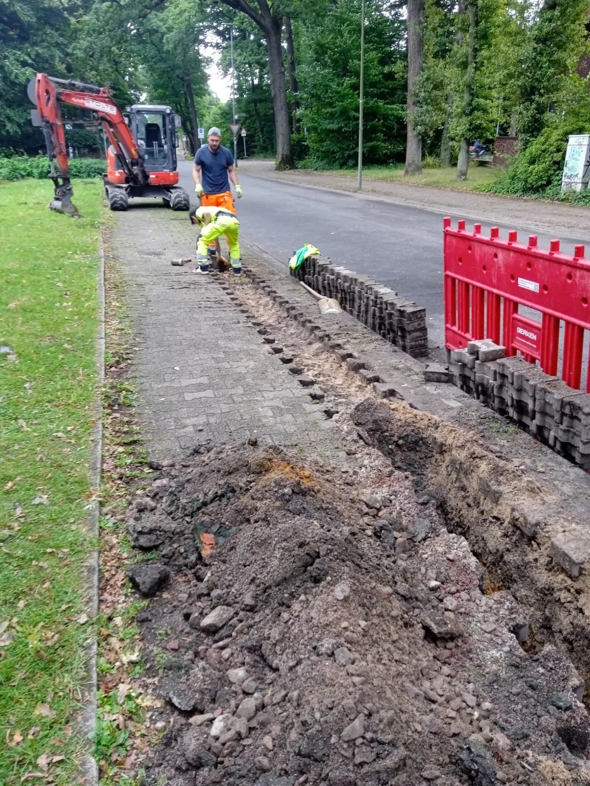 Bagger und Team bei Grabenarbeiten neben einer Straße