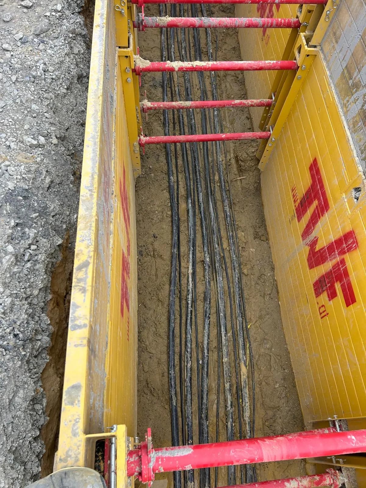 Leitungsbündel im Graben zwischen gelben Verbaukästen mit roten Spindeln