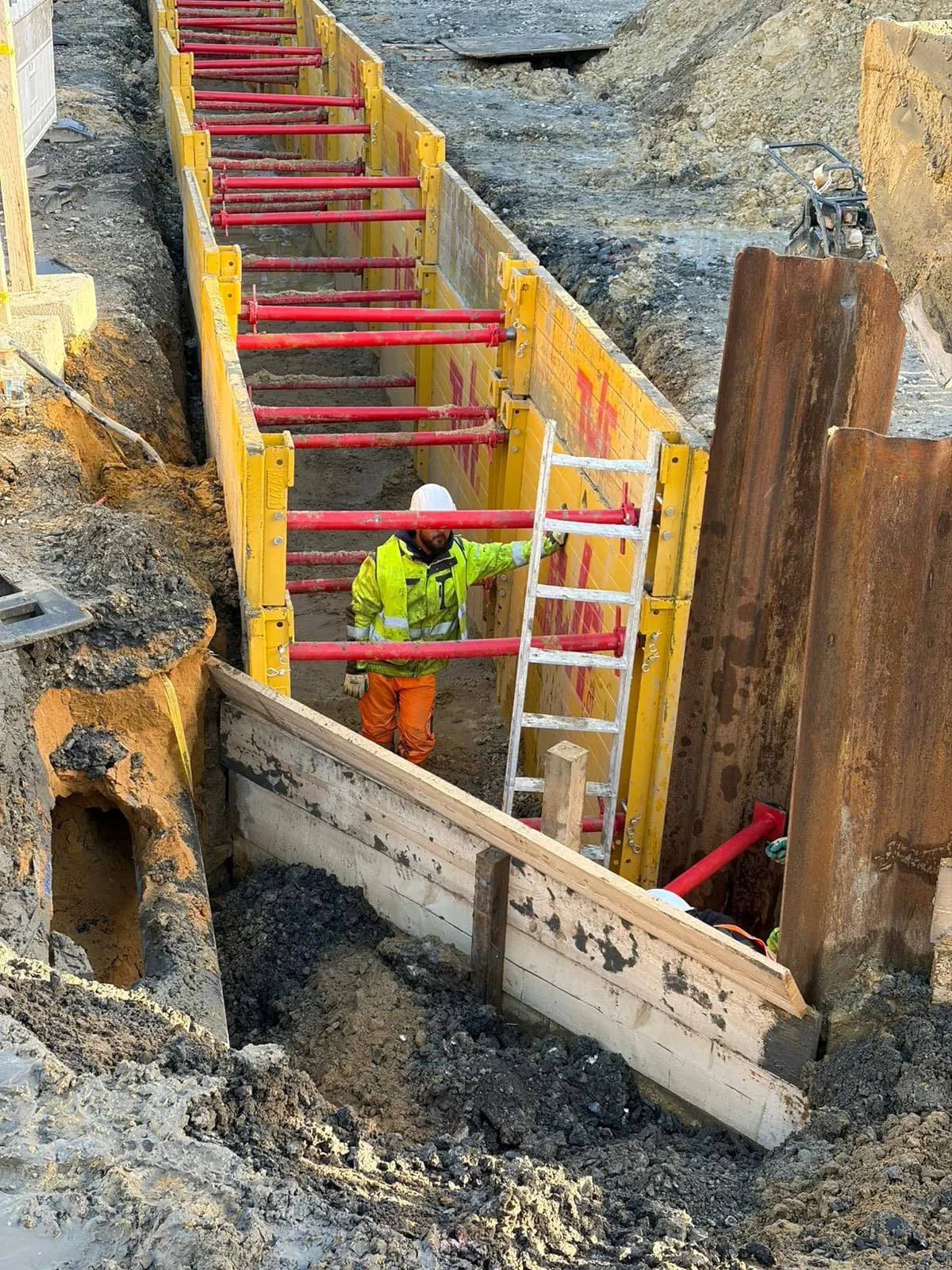 Arbeiter steigt über eine Leiter in den verbauten Graben