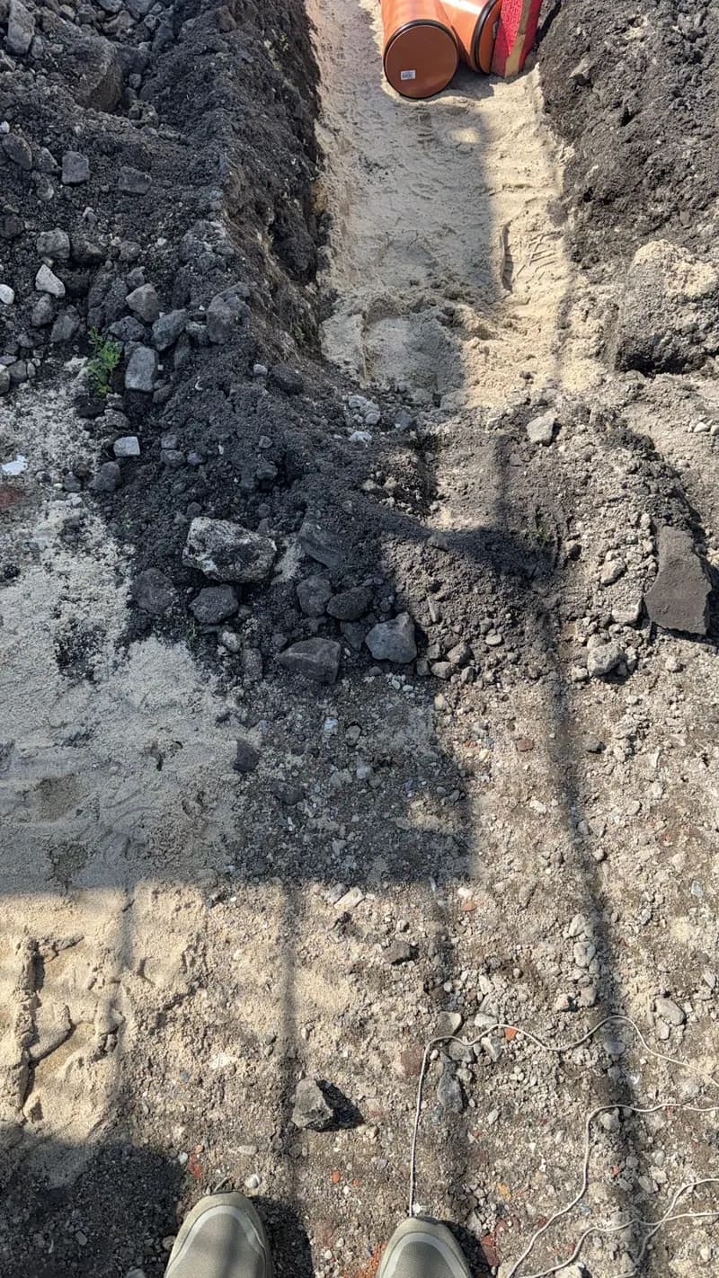 Grabenarbeiten mit bereitliegendem Rohr auf einer Gewerbebaustelle