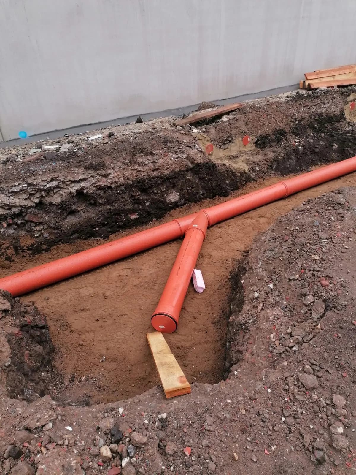 KG-Rohrleitung mit Abzweig in der Baugrube vor einem Neubau