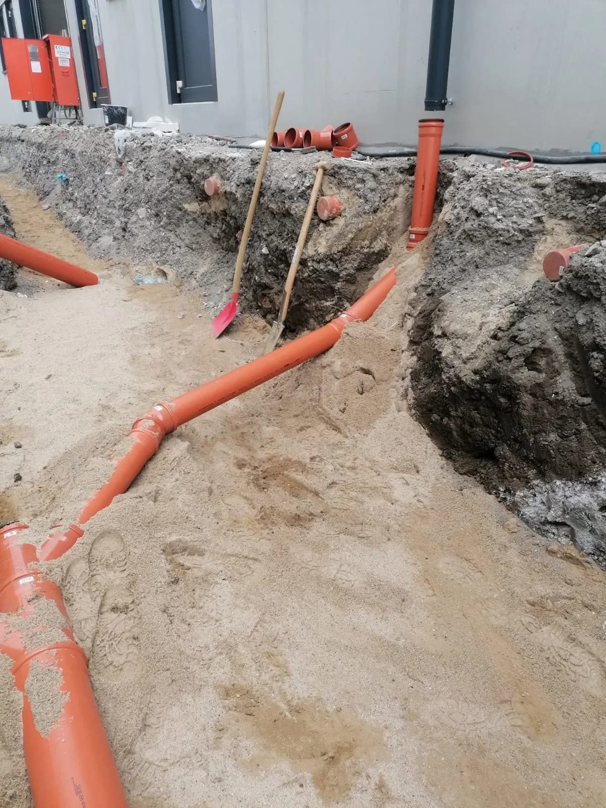 Rohrleitung mit Abzweig im Sandbett vor dem Gebäude